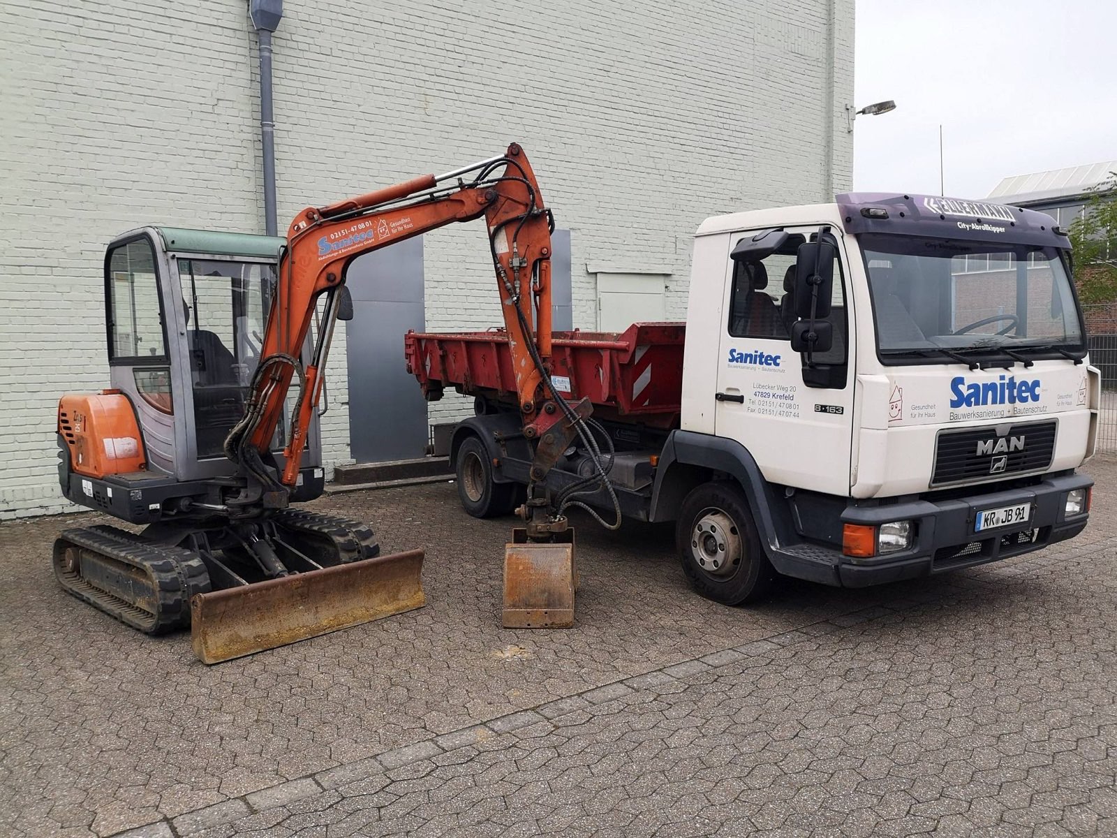 Minibagger und MAN-Kipper mit Sanitec-Beschriftung auf dem Betriebshof der Sanitec GmbH in Krefeld