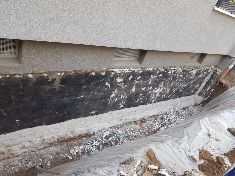 Kelleraußenwand mit schadhafter schwarzer Altabdichtung und Salzausblühungen im geöffneten Graben