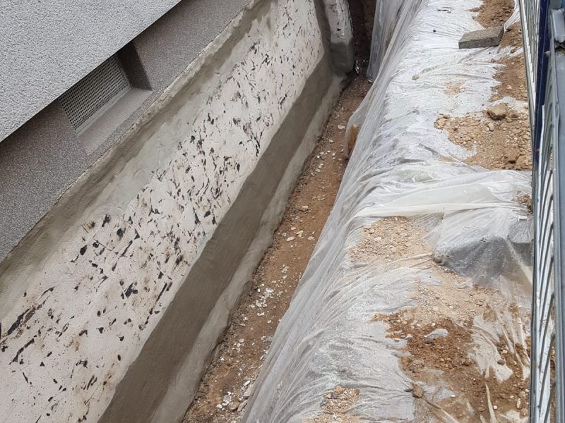 Entlang der Hauswand ausgehobener Arbeitsgraben mit Abdeckfolie zur Freilegung der Kellerwand