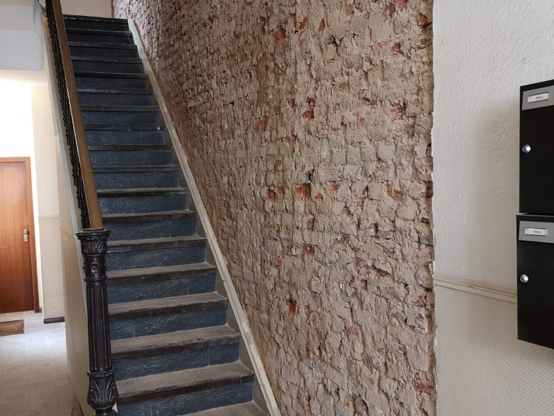 Freigelegtes Ziegelmauerwerk im Hausflur neben der Treppe während der Putzsanierung