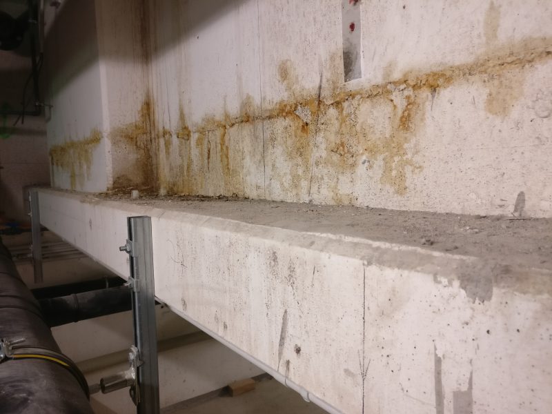 Betonbauteil mit Feuchteschaden und Rostfahnen, davor ein Gerüstrohr