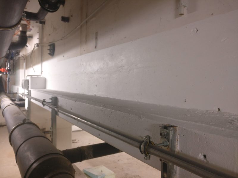 Helle Betonwand mit Rohrleitungen im Technikraum, ohne Feuchtigkeitsspuren nach der Rissverpressung