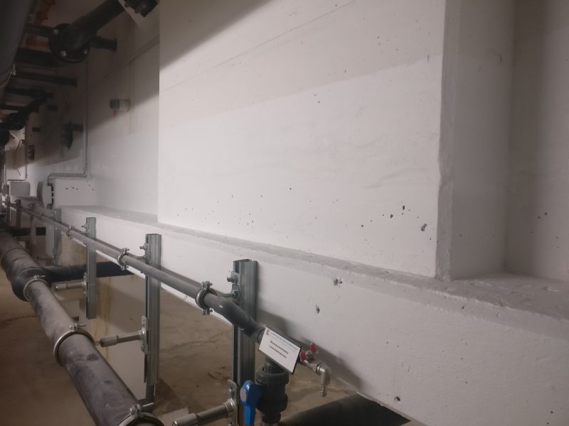 Betonwand und Rohrleitungen im Technikraum nach der Abdichtung, trockene Wandfläche