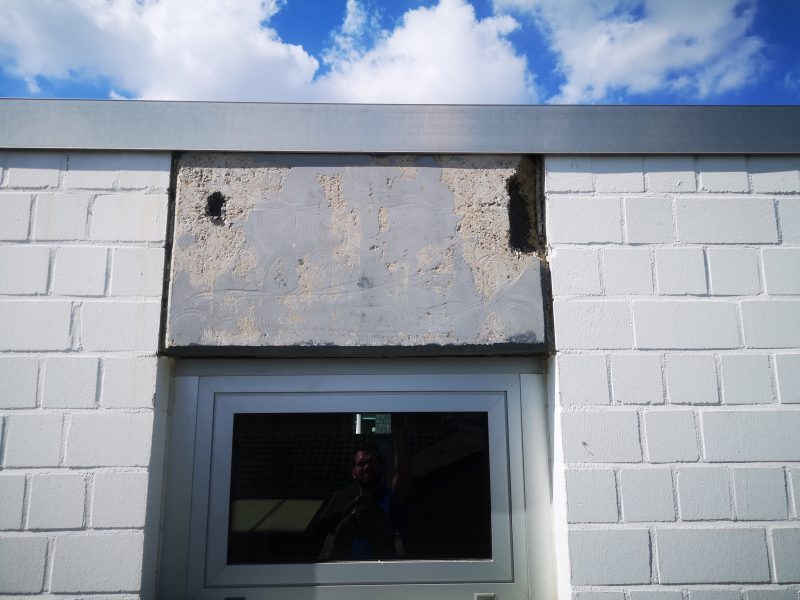 Nahaufnahme eines Fenstersturzes mit abgeplatztem Beton und freiliegenden Fehlstellen
